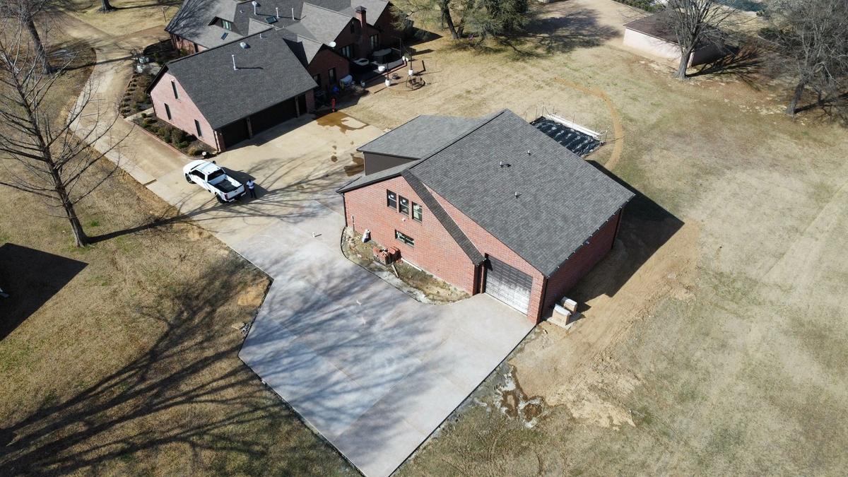 Aerial view of a finished brick garage beside a house, with a truck and person in the driveway.
