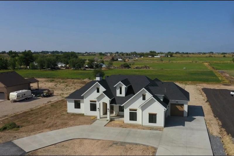 Finished single-story house with a black roof and light exterior, an RV trailer and ATV parked nearby on a rural property.