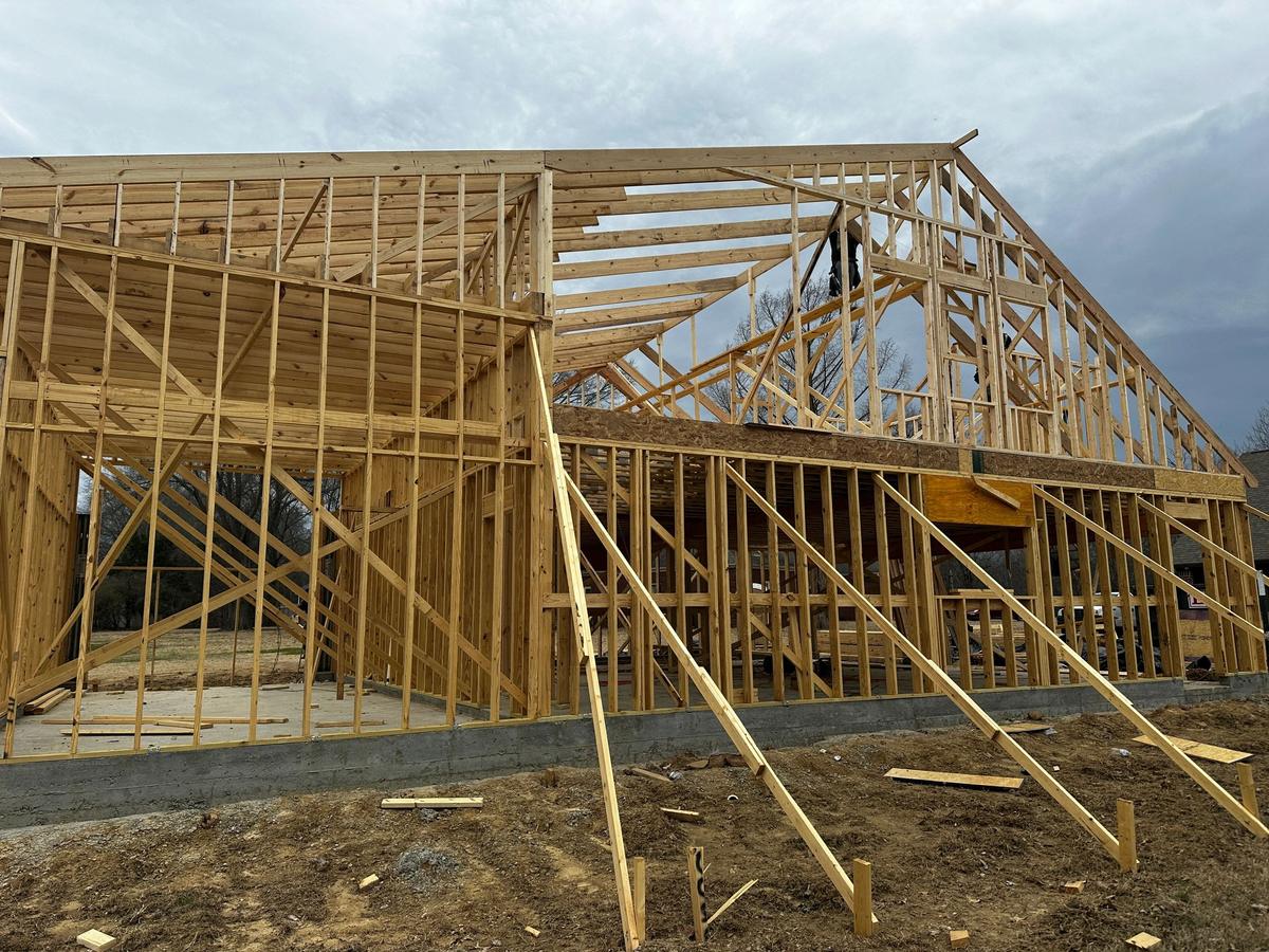 Closer view of the same wood-framed building, showing open stud walls and roof trusses against a cloudy sky.