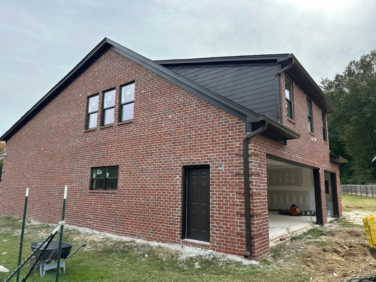 Two-story brick building with black trim and a black door, an open garage bay showing interior drywall inside.