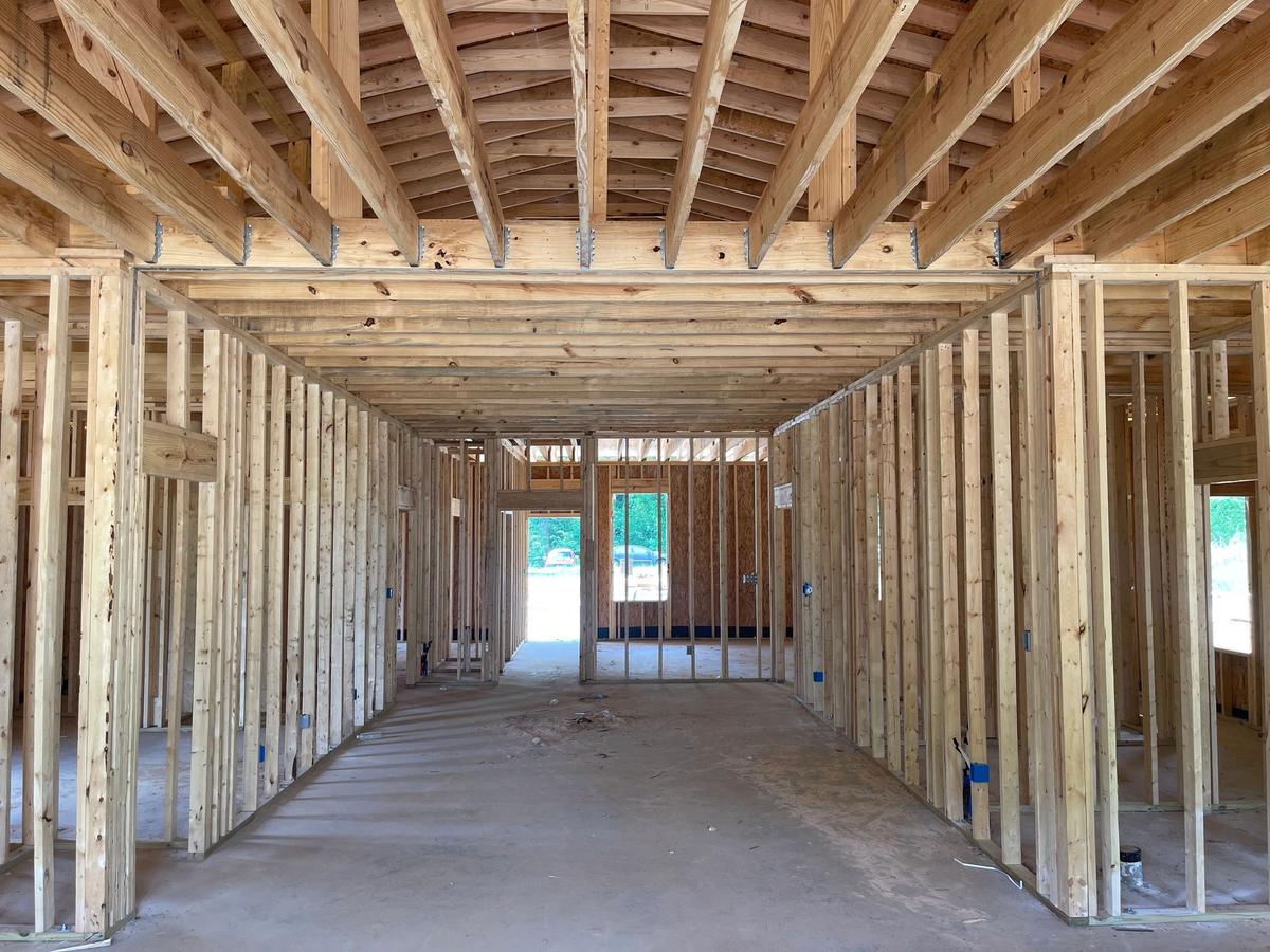 View down a hallway of newly framed stud walls, with two parked cars visible through an exterior opening.